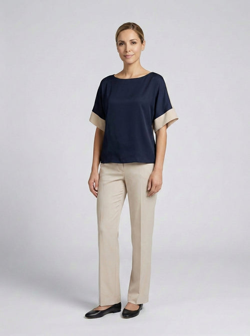 Dama con blusa azul marino de cuello barco y puños beige con pantalón beige, recepción de resort.