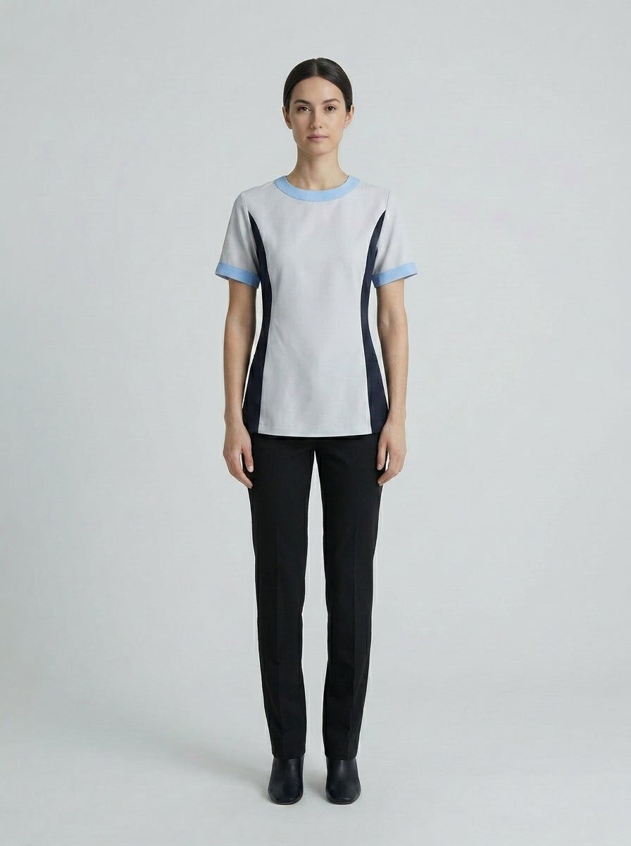 Dama con blusa gris de cuello azul cielo y paneles azul marino con pantalón negro para camarista de hotel.