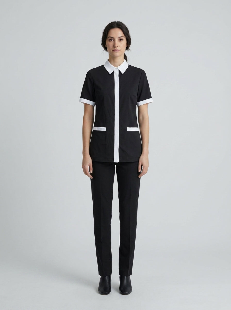 Dama con blusa negra de cuello blanco y placket blanco con pantalón negro para camarista de hotel.