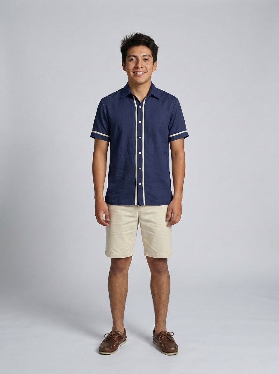 Caballero con camisa azul marino de lino y vivo crema con bermuda beige para personal de alberca de resort.