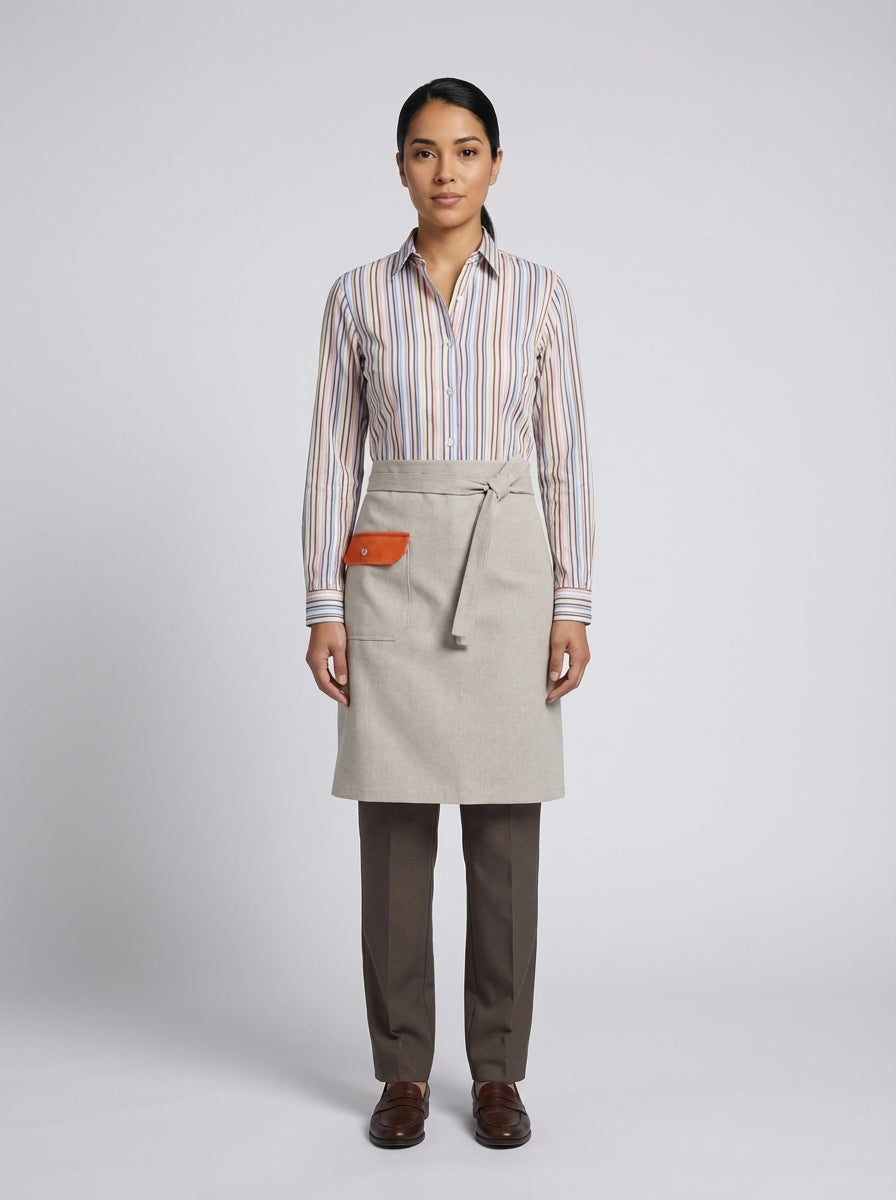 Dama con camisa de rayas multicolor y mandil arena con bolsillo naranja para anfitriona de restaurante.