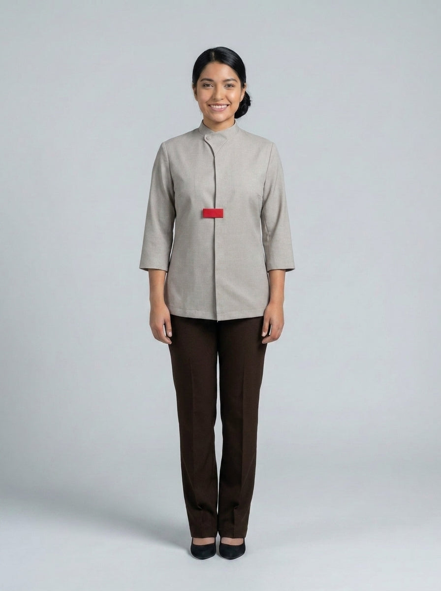 Dama con casaca gris de cuello mao y placa roja sobre pantalón café para anfitriona de restaurante.
