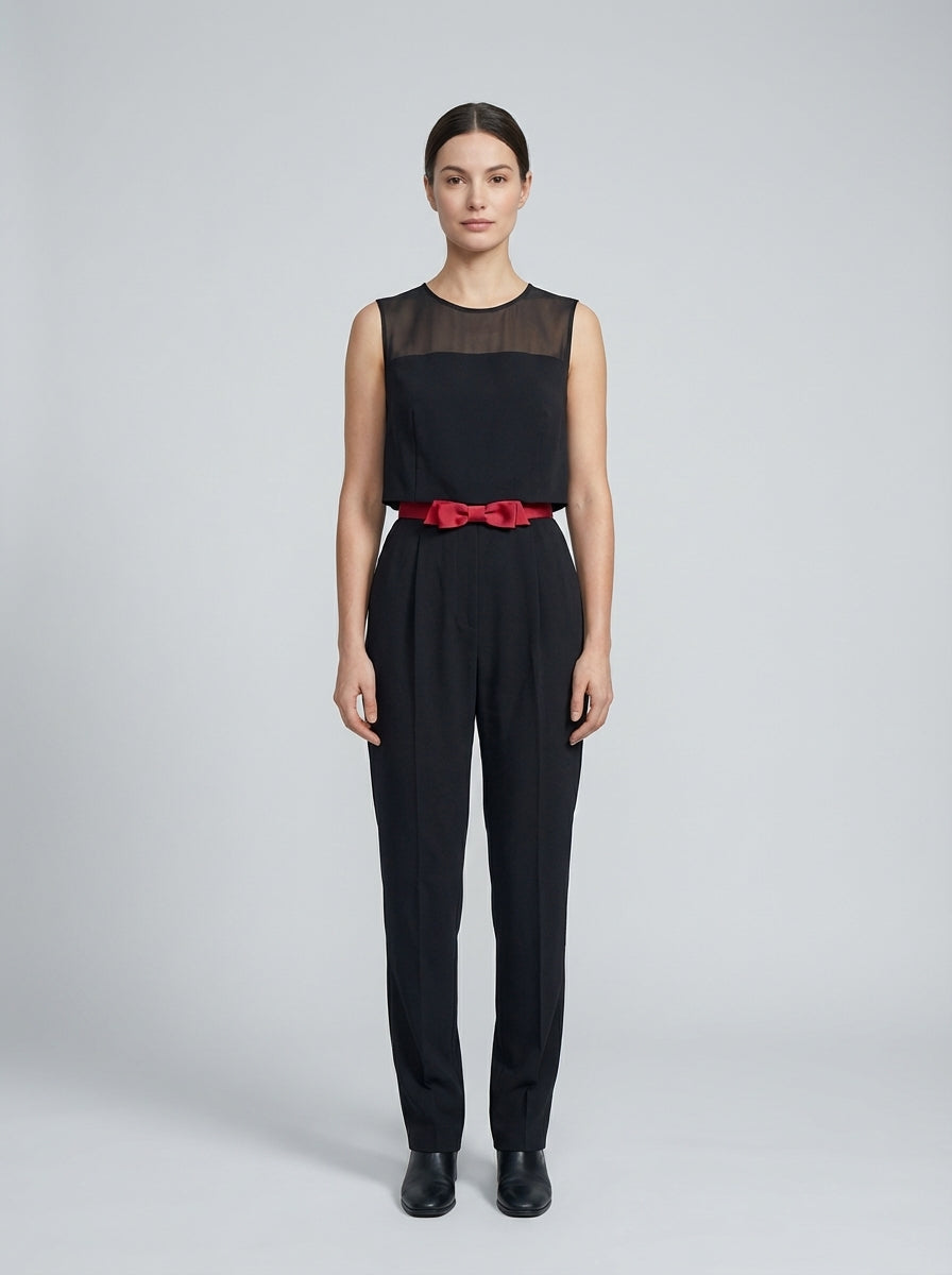 Dama con jumpsuit negro de panel de gasa y cinturón con moño rojo para anfitriona de restaurante.