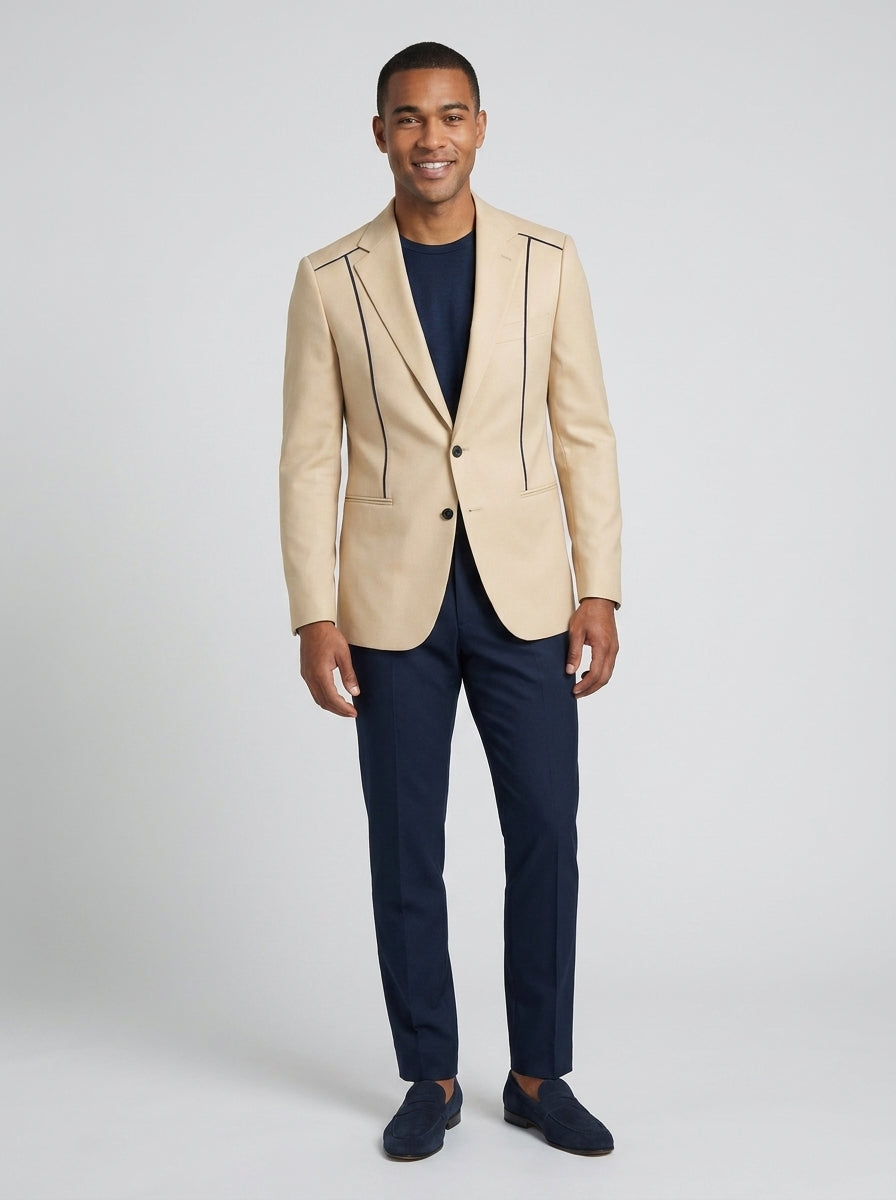 Caballero con saco beige de vivo negro sobre camiseta y pantalón azul marino, para recepción de resort.