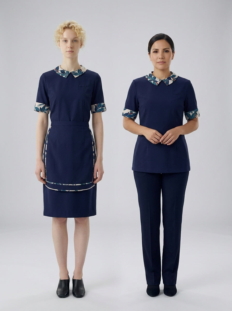 Dos damas con uniforme azul marino de cuello floral, una con vestido y otra con blusa y pantalón, para camarista de hotel.