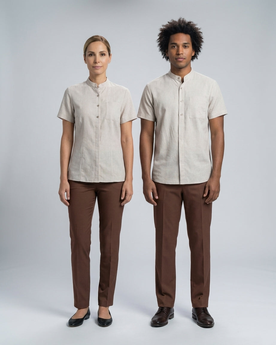 Dama con blusa beige de cuello mao y caballero con camisa beige de cuello mao con pantalón café para camarista y mozo de hotel.