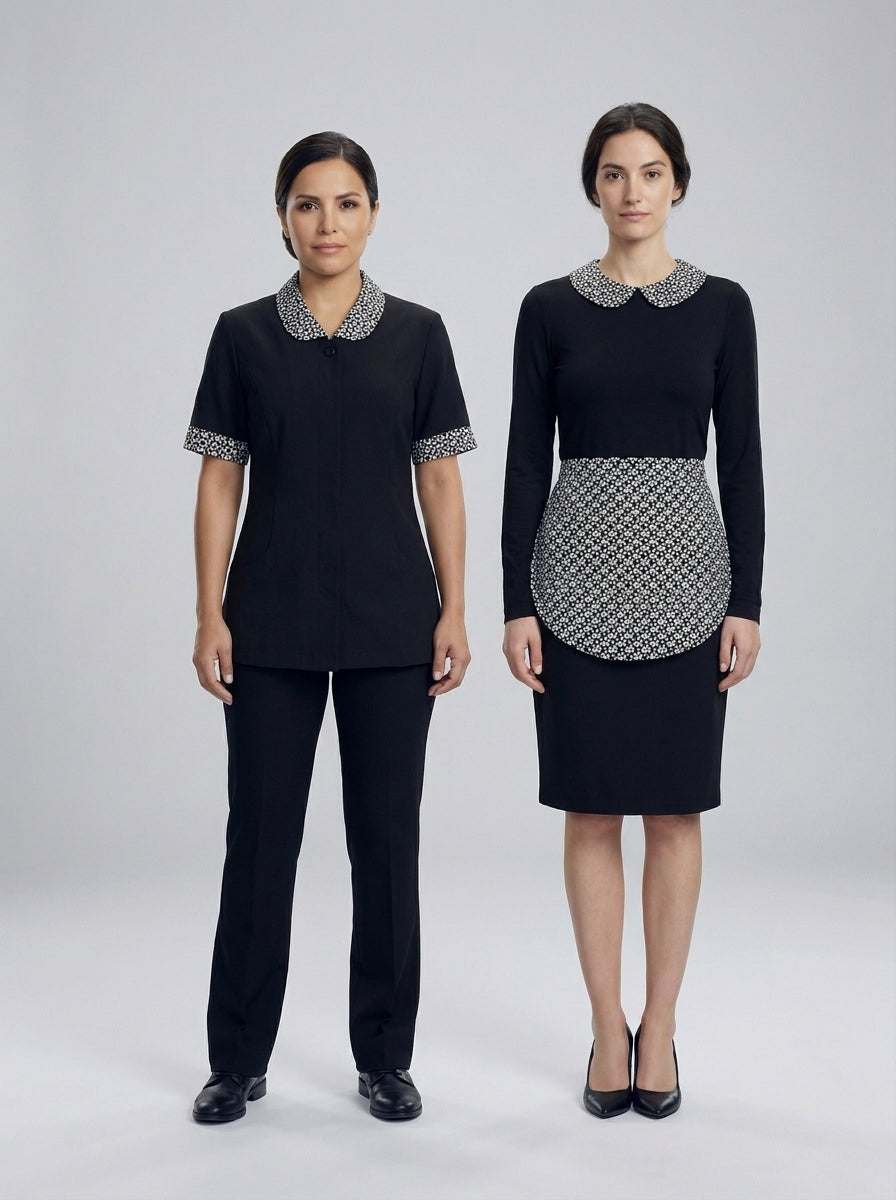 Dos damas con uniforme negro de cuello floral, una con pantalón y otra con mandil y falda, para camarista de hotel.